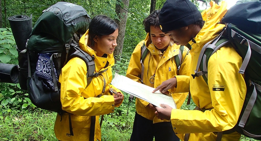 Three students wearing rain jackets and backpacks examine a map.